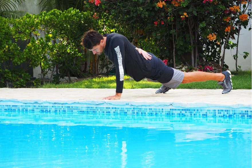 Man performing one-arm push-up next to an outdoor pool.