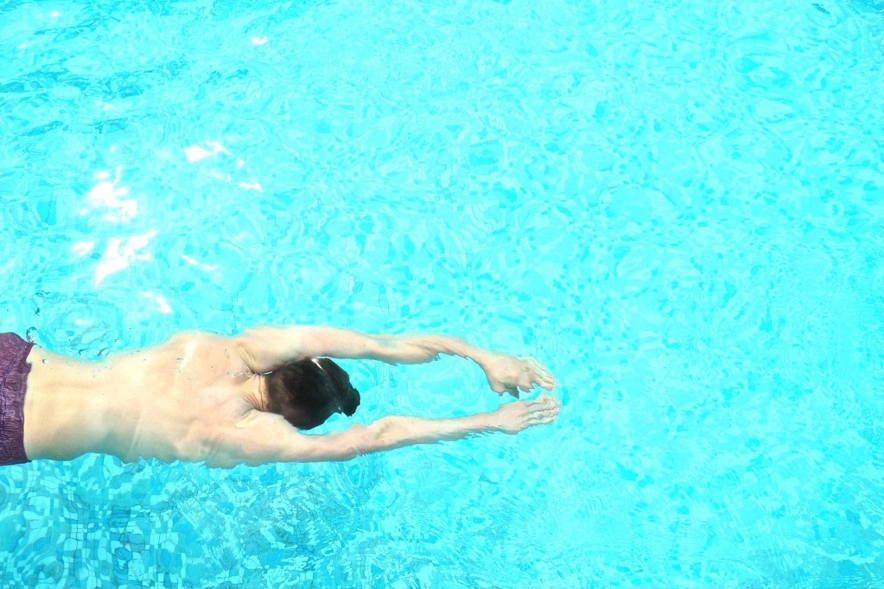Shirtless man swimming underwater in a bright blue pool