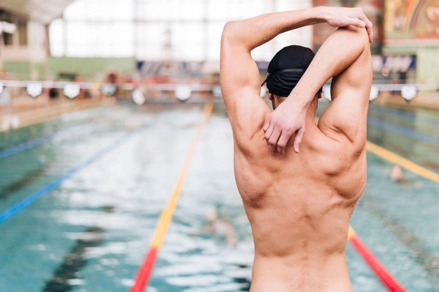 Back view of a man stretching his arm by a swimming pool.